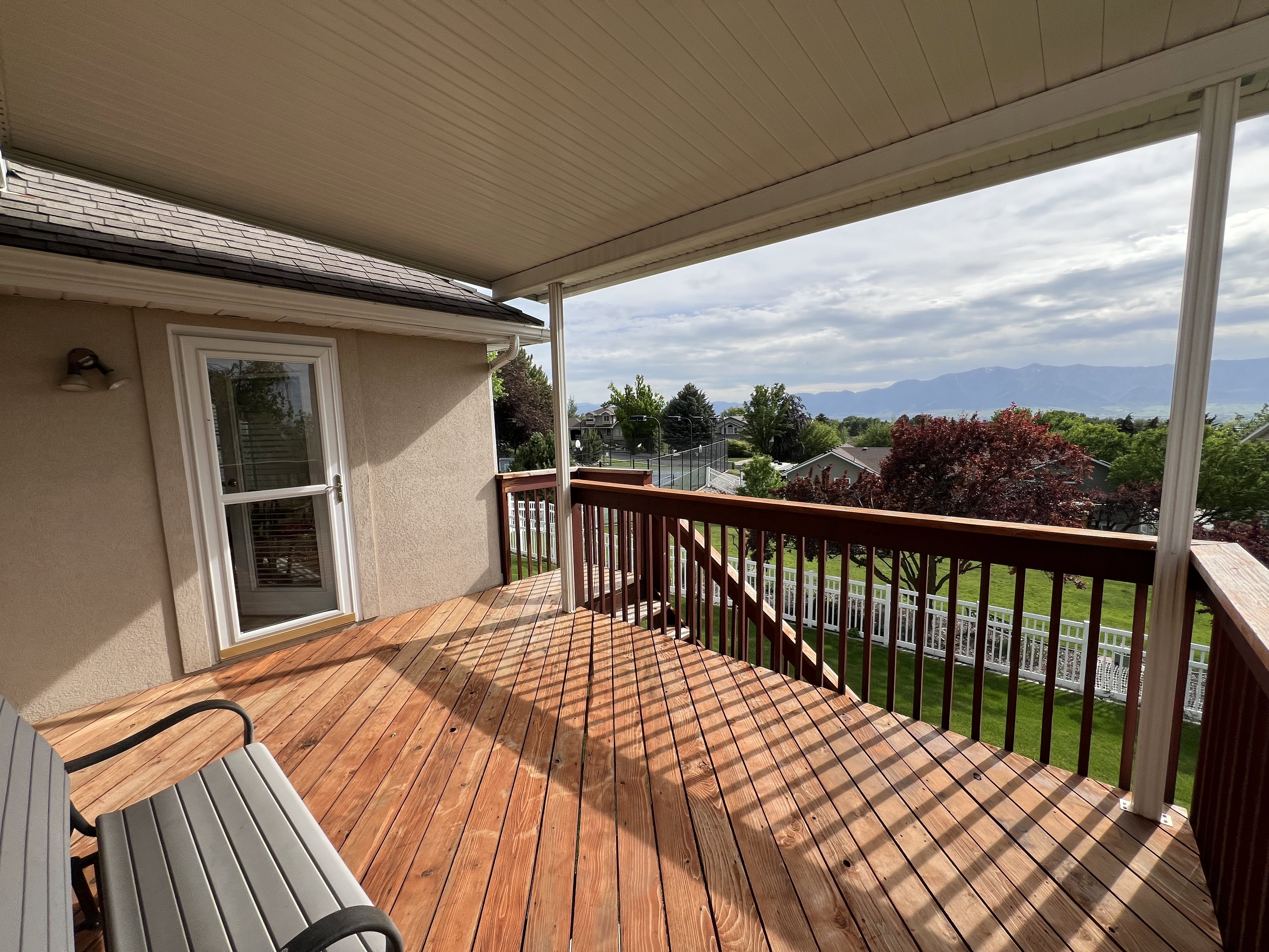 Covered outdoor deck with stained wood flooring, dark wood railings, and mountain scenery