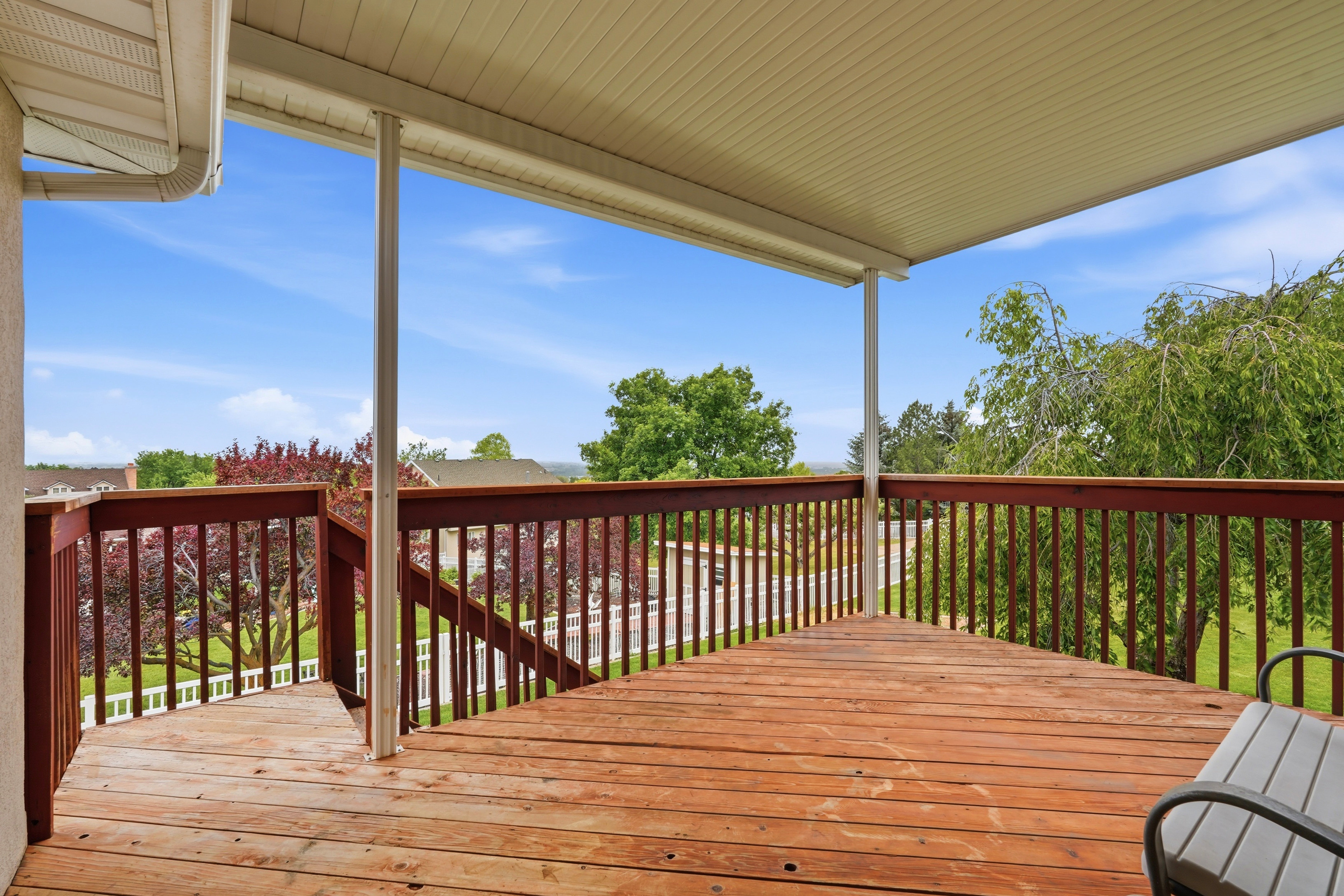 Spacious outdoor deck featuring natural wood-finish flooring, a covered patio, and stained wood railing with balusters