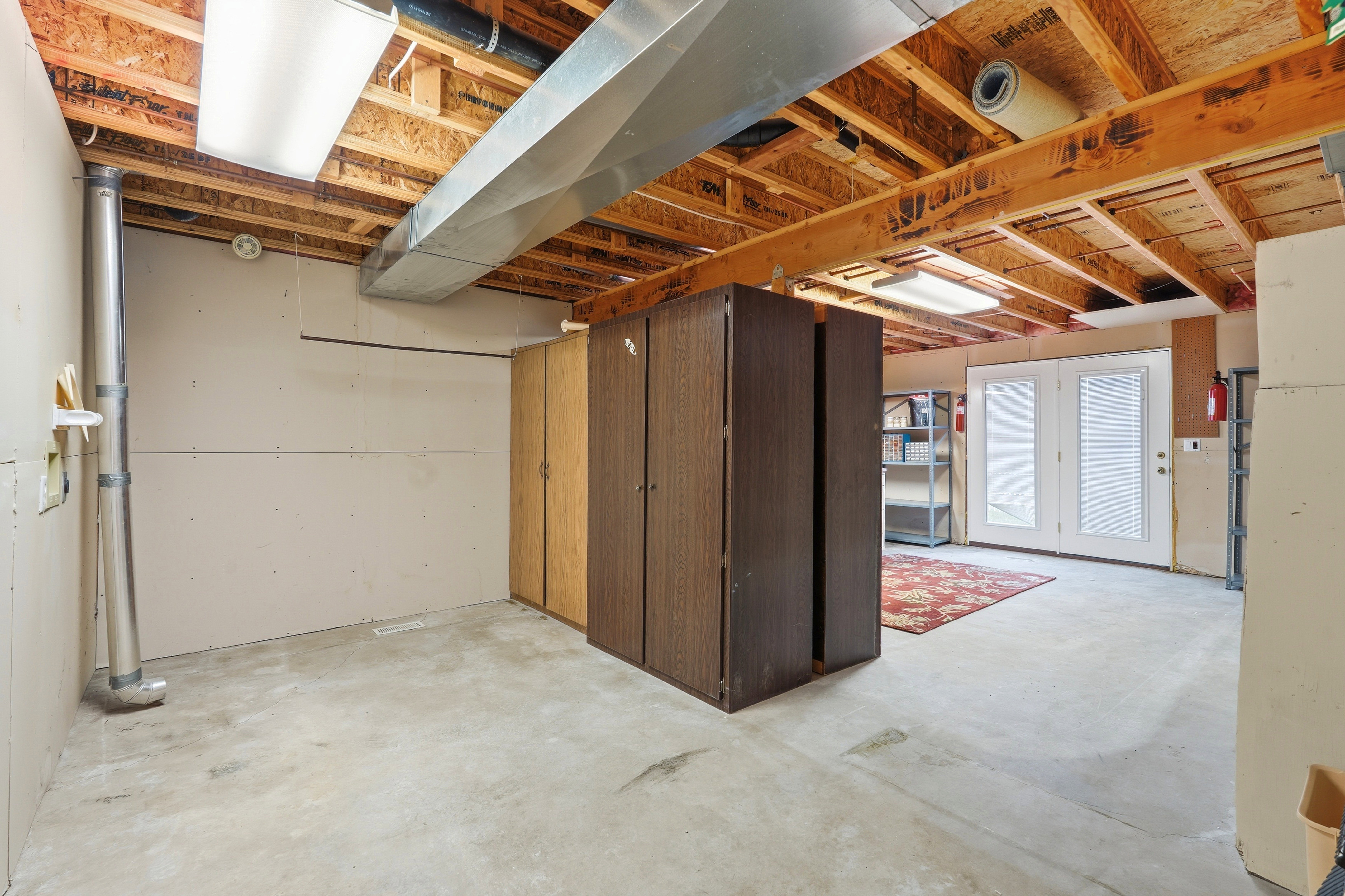 Unfinished basement featuring exposed wood joists, concrete flooring, and French doors