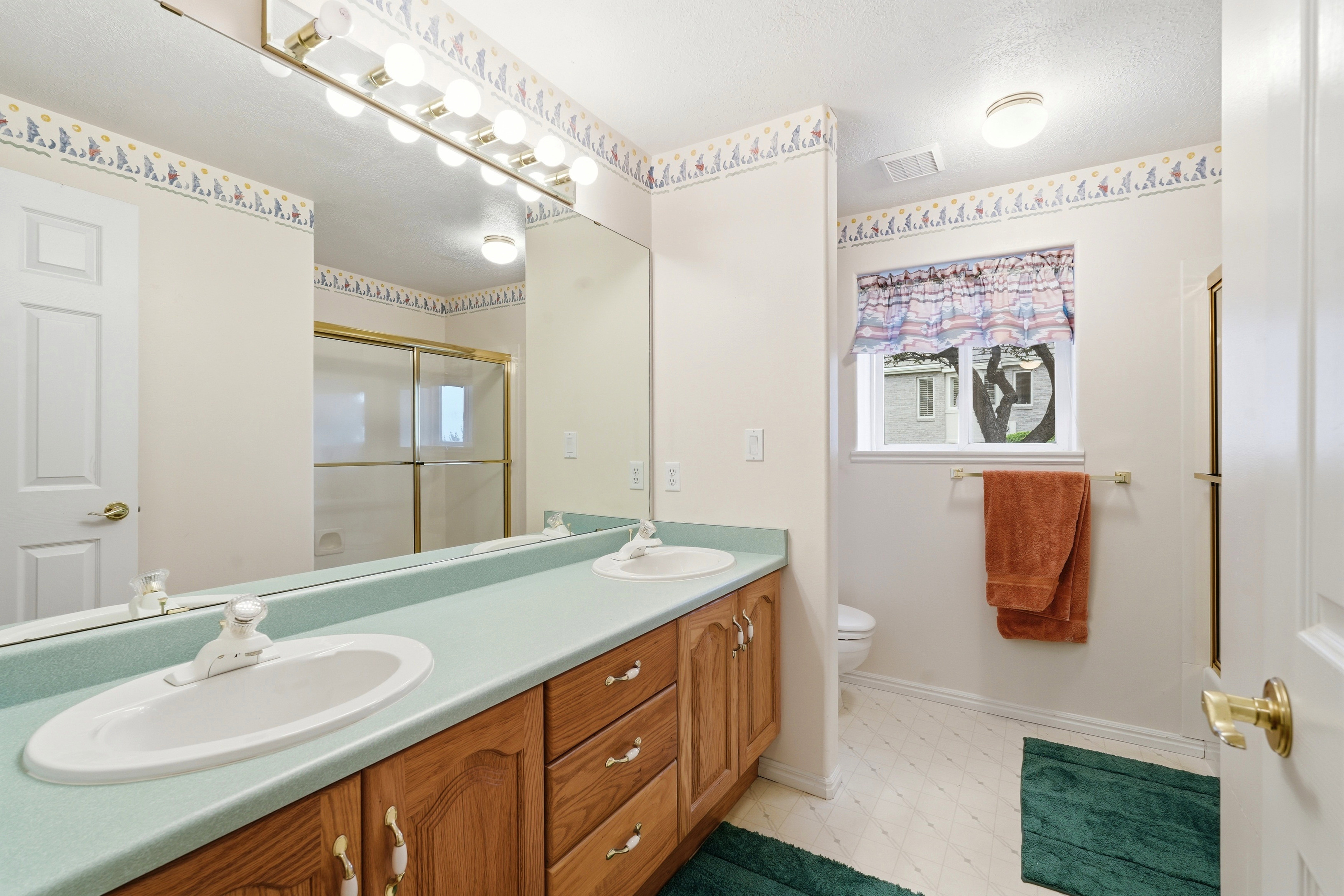 Double vanity with dual undermount sinks, light green countertops, and wood-finish cabinetry