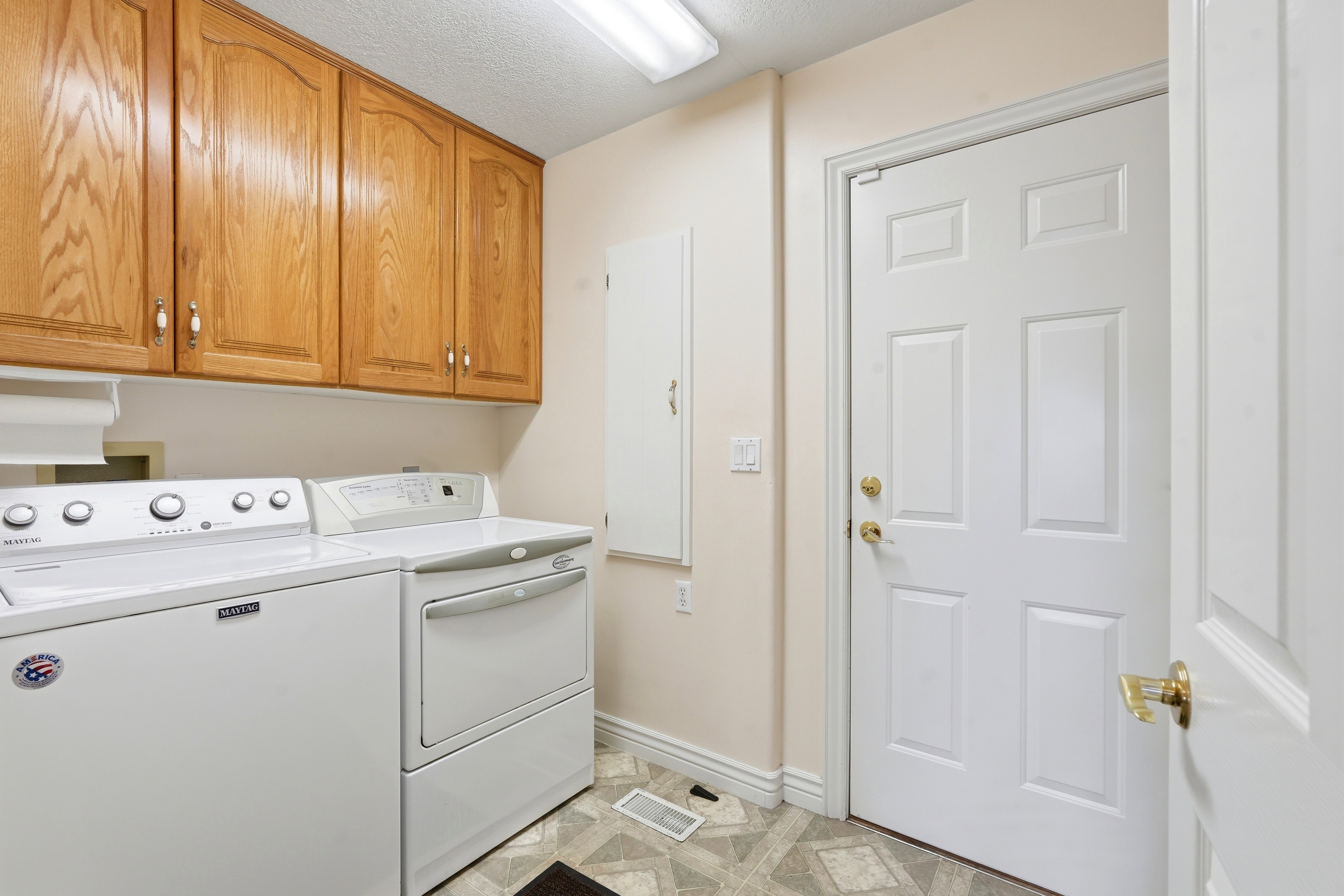 Laundry area featuring overhead wood cabinetry with decorative pulls, light-toned wall paint, and patterned sheet vinyl flooring
