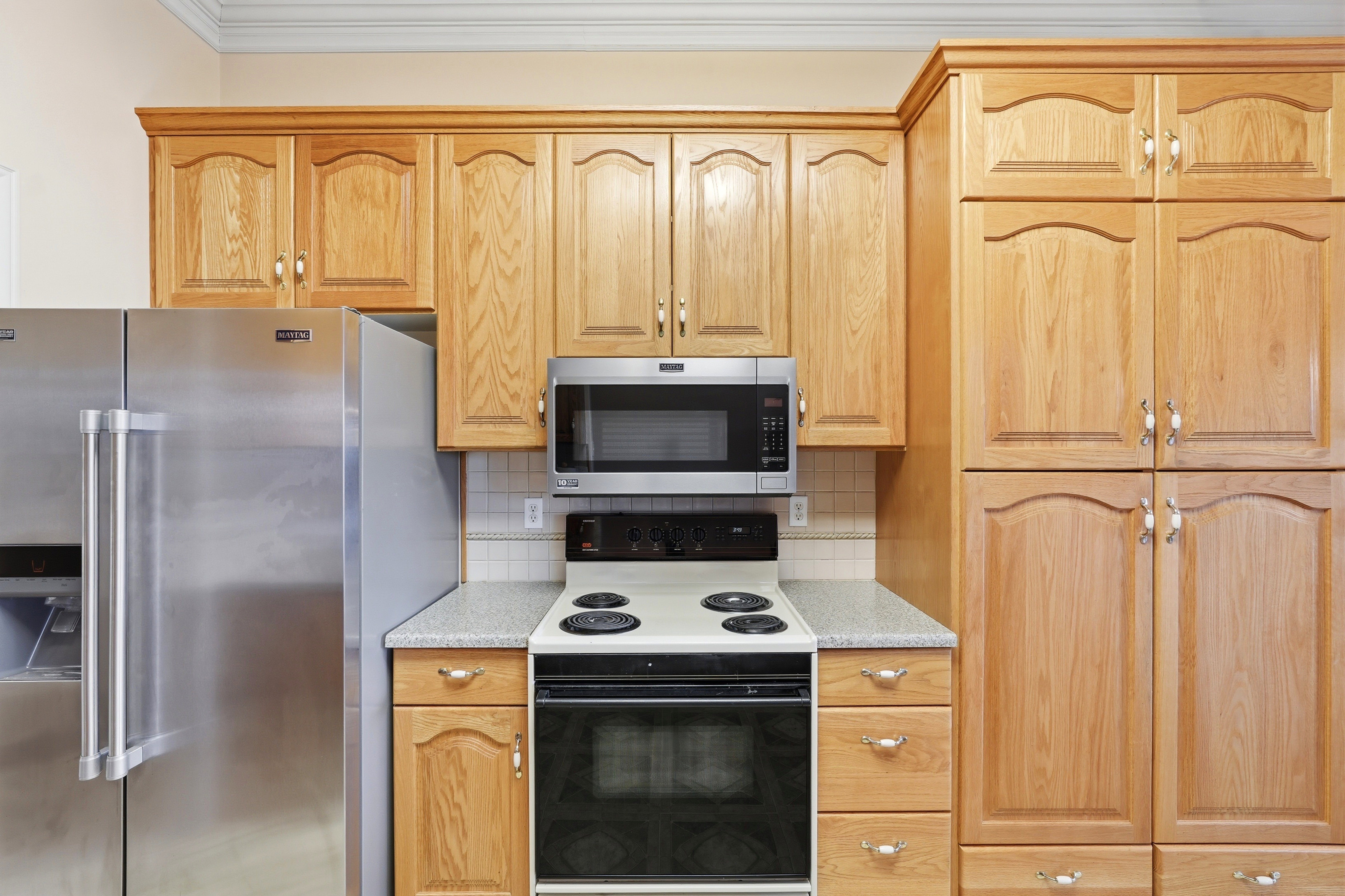 Full kitchen featuring light wood cabinetry, stainless steel appliances, a built-in microwave, a tile backsplash, and light-toned countertops