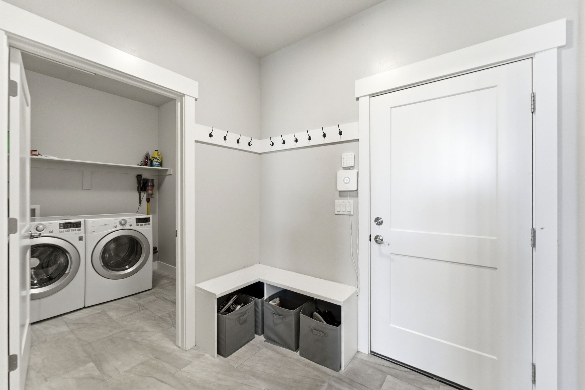 Dedicated utility space featuring a built-in bench with storage, wall-mounted coat hooks, and a laundry area with shelving.