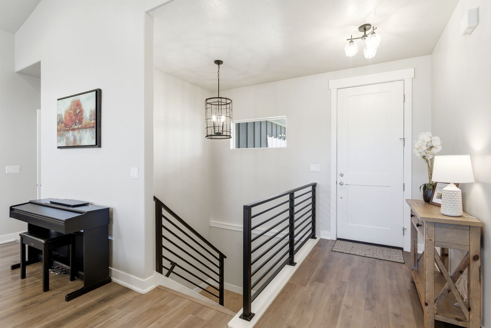 Inviting foyer featuring wood-finish flooring, a contemporary black metal railing, and a prominent white entry door.