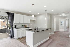 Open concept kitchen featuring white shaker cabinetry, dark countertops, a subway tile backsplash, and a central island with an undermount sink