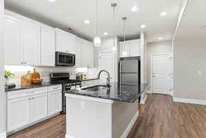 Contemporary kitchen featuring white cabinetry, dark stone countertops, stainless steel appliances, and wood-finish flooring