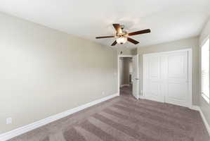 Bedroom featuring plush carpet flooring, a ceiling fan with integrated lighting, white baseboards, and a double-door closet with panel detailing