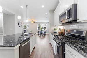 Modern kitchen featuring dark granite countertops, white cabinetry, stainless steel appliances, and wood-finish flooring
