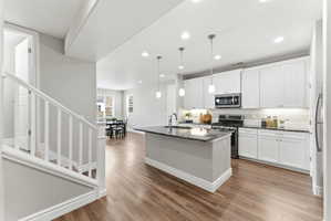 Kitchen featuring an island with a dark countertop, white shaker-style cabinetry, stainless steel appliances, subway tile backsplash, and wood-finish flooring