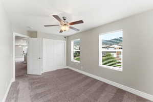 Spacious bedroom featuring neutral wall tones, two windows with blinds, a ceiling fan with light fixture, and plush carpet flooring
