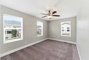 Spacious room featuring multiple windows with blinds, a ceiling fan with light fixture, neutral wall paint, and plush carpet flooring
