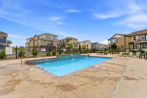 Outdoor swimming pool with integrated water features, surrounded by a spacious concrete deck and black metal fencing