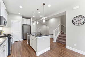 Kitchen featuring wood-finish flooring, white cabinetry, dark countertops, a central island with sink, and stainless steel appliances