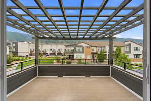 Expansive outdoor deck featuring a slat pergola, concrete-style flooring, dark siding, and black metal railings