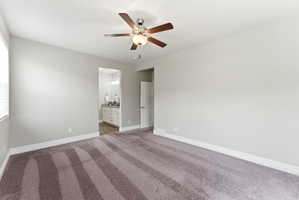 Spacious room featuring neutral-toned walls, plush carpet flooring, a ceiling fan with integrated lighting, and white baseboards