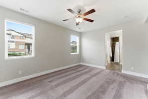 Carpeted bedroom featuring two windows with horizontal blinds, a ceiling fan with integrated lighting, and an entryway to an attached bathroom with tiled flooring and a shower stall