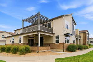 Contemporary multi-level exterior with a pergola-covered upper balcony, covered porch, large windows, and a brick base