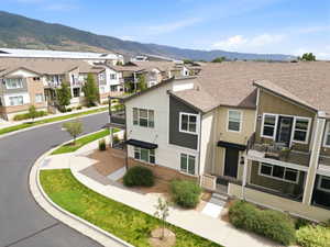 Multi-level townhome featuring a neutral-toned exterior with dark accents, a front porch, and an upper-level balcony