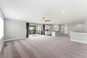 Expansive living area with neutral carpeting, recessed lighting, and a ceiling fan