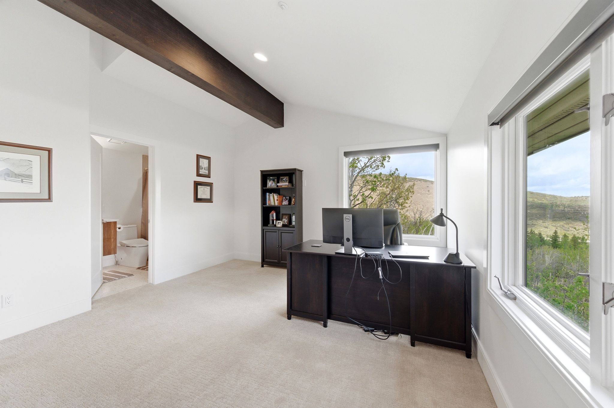 Vaulted ceiling room with an exposed dark wood beam, light carpet flooring, and white walls