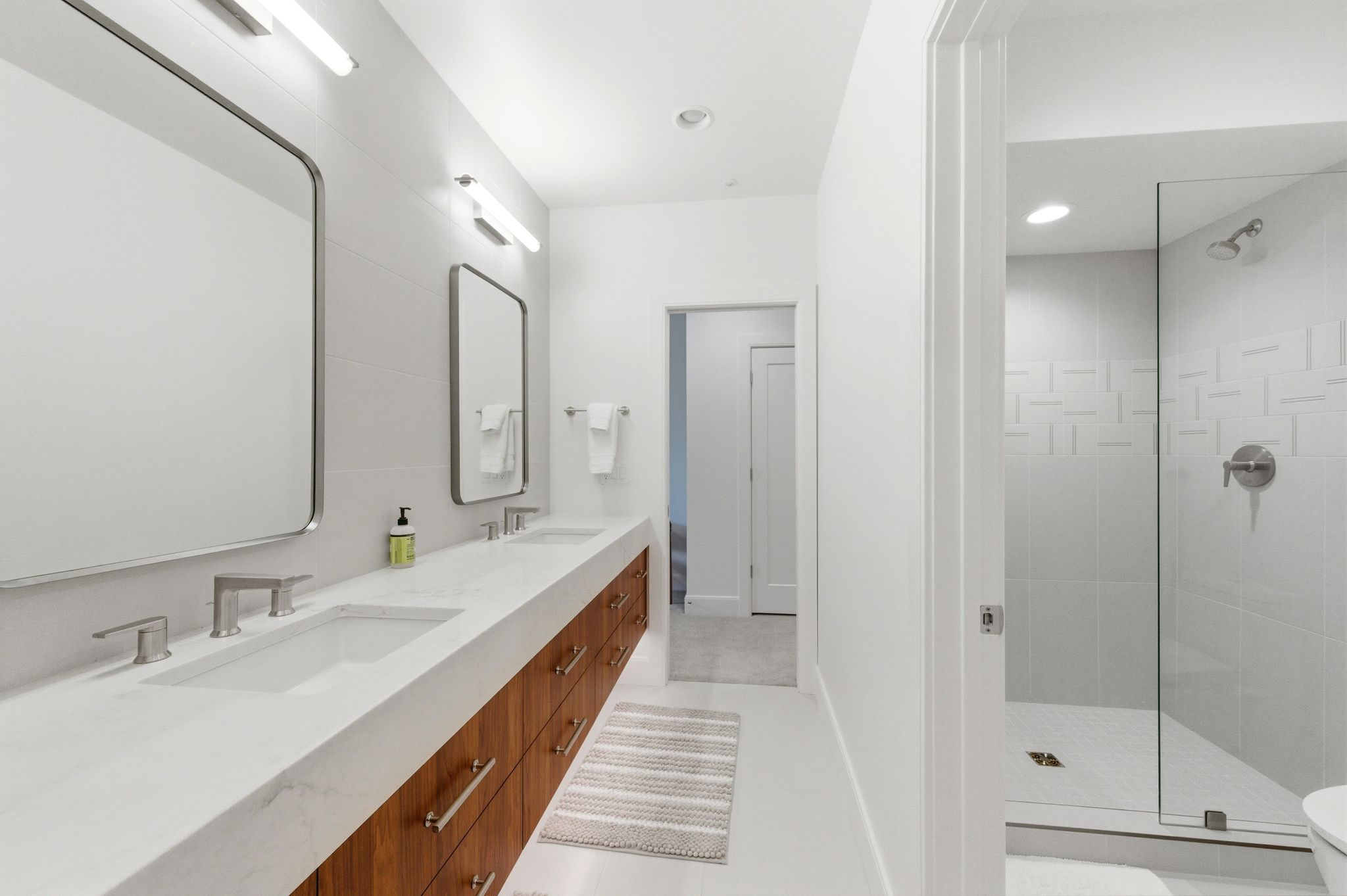 Bathroom featuring a dual vanity with a light-toned countertop and wood-finish cabinetry, rectangular undermount sinks, and wall-mounted mirrors