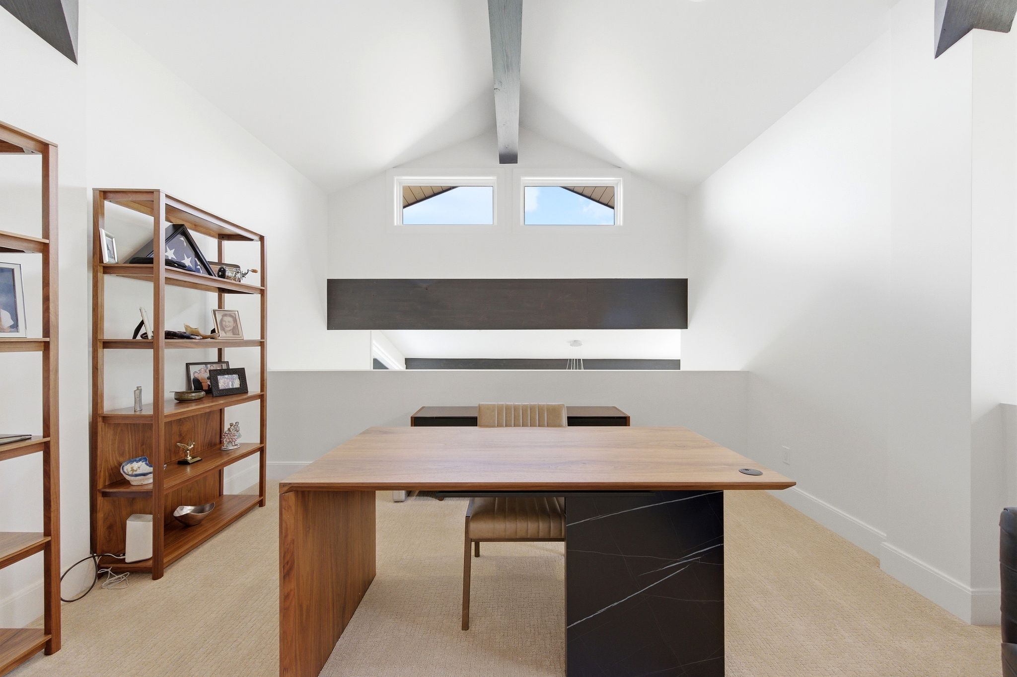 Loft space featuring a vaulted ceiling with exposed beam, dual clerestory windows, and architectural half-wall
