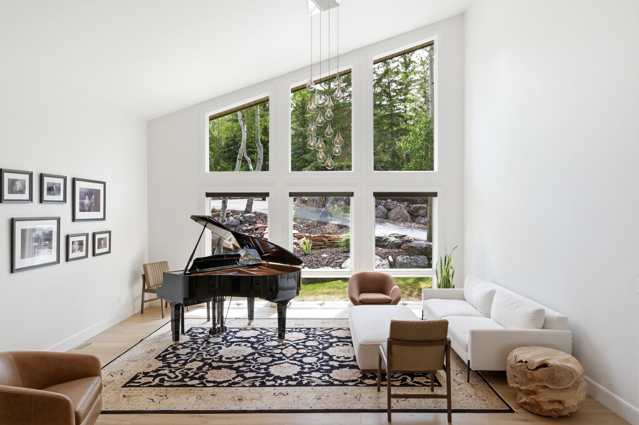 Vaulted ceiling living area featuring a multi-pane window wall, light wood-finish flooring, and a contemporary chandelier