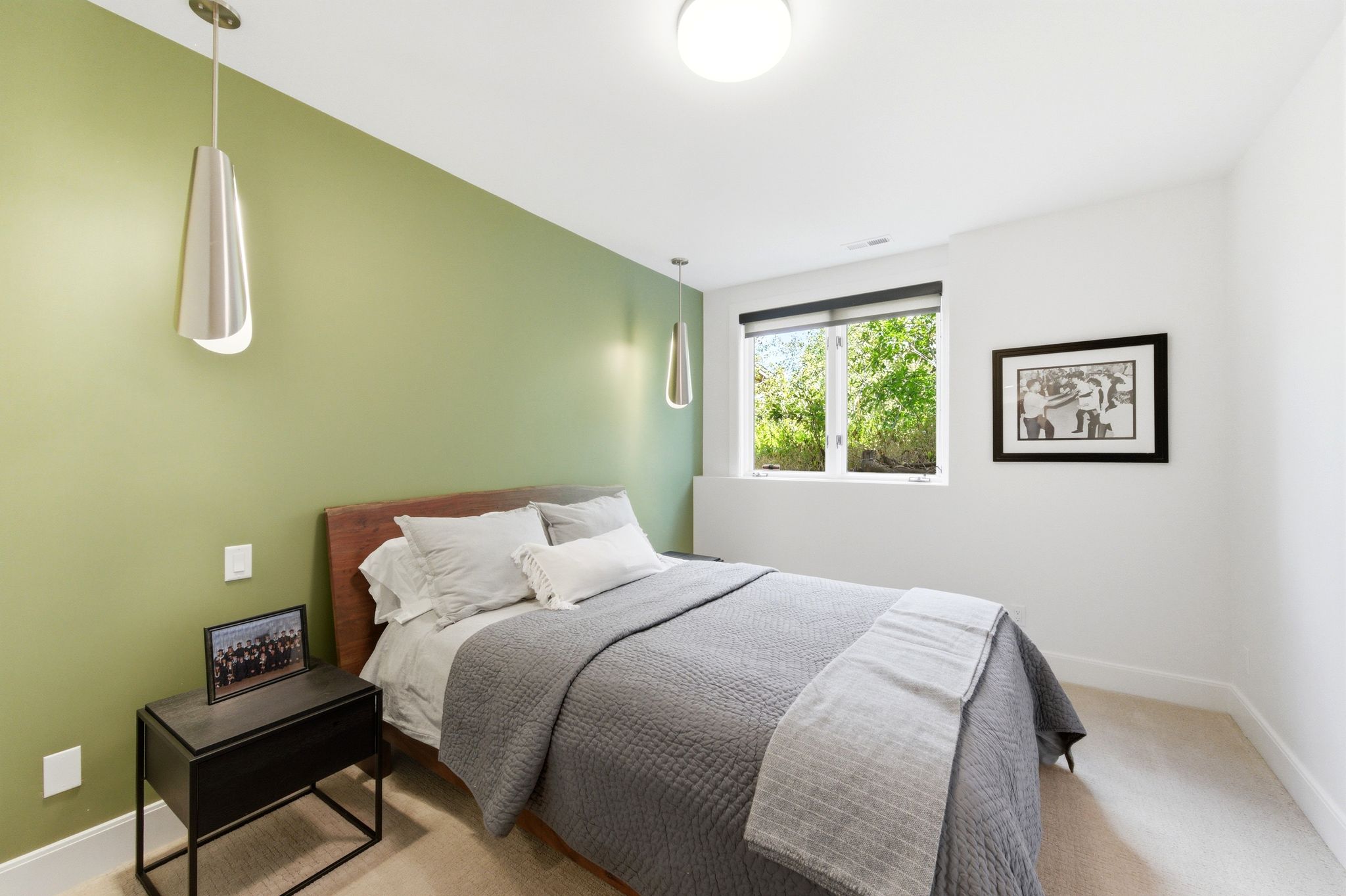 Bedroom featuring a contrasting accent wall, two pendant light fixtures, and a large window with roller shades