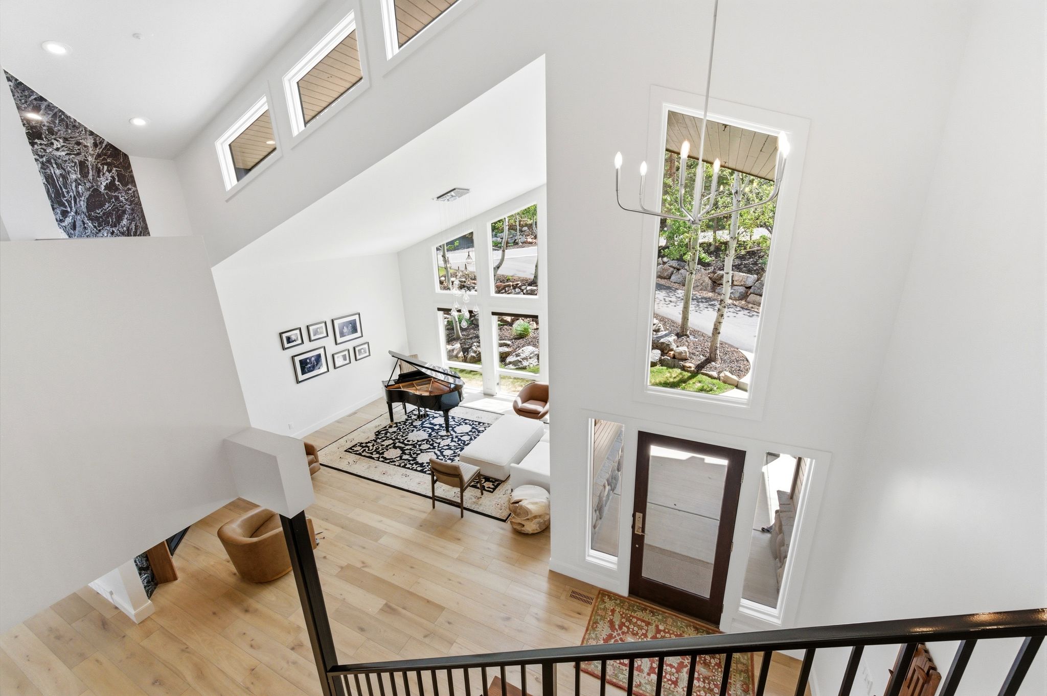 Double-height entry foyer featuring a modern chandelier, light wood-finish flooring, and a dark wood-finish entry door with clear glass panels