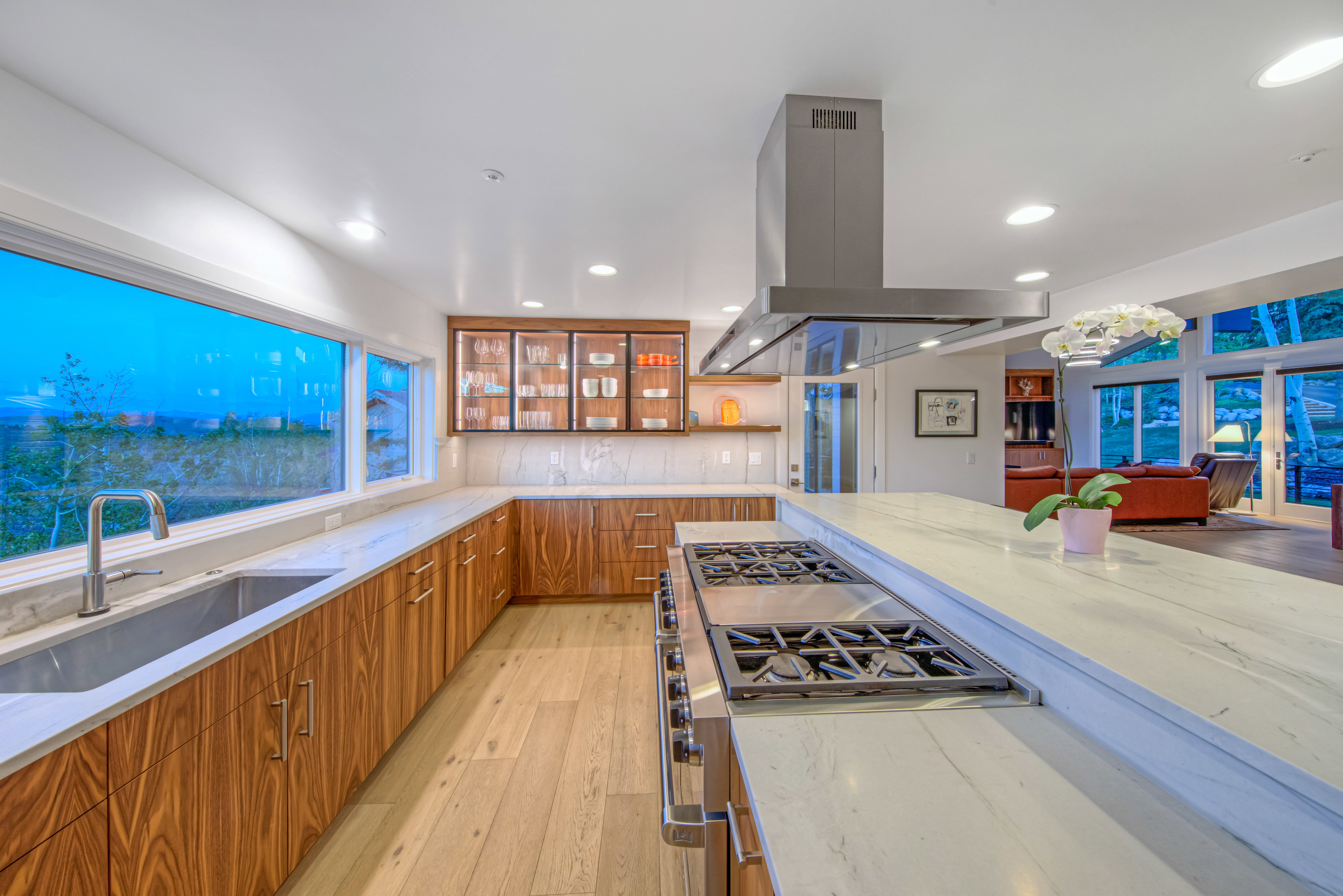 Contemporary kitchen featuring a large island with a built-in gas range, extensive wood-finish cabinetry, light-toned countertops, a stainless steel sink, and a panoramic window