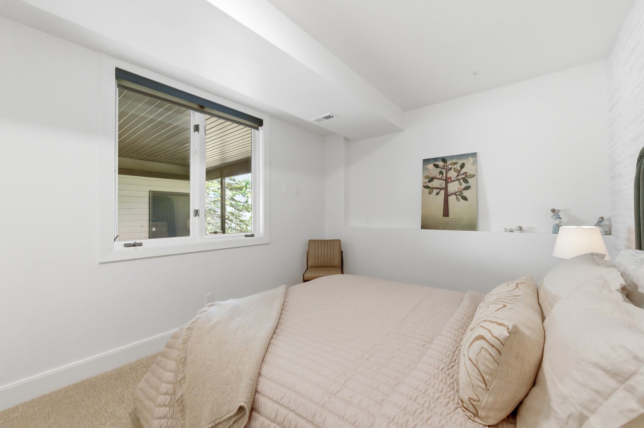 Bedroom with light-colored carpeting, white baseboards, and a window with a dark roller shade