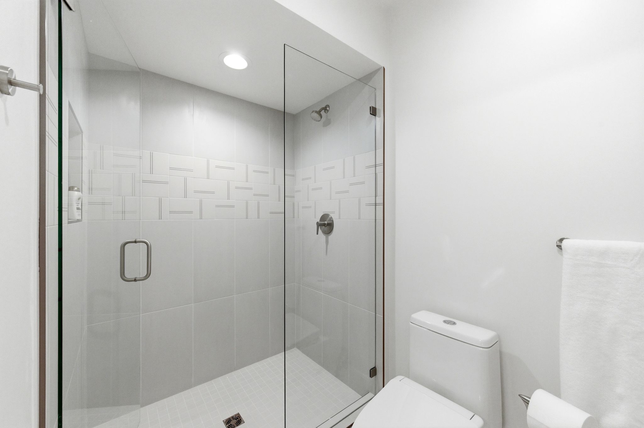 Walk-in shower featuring a frameless glass enclosure, a tiled accent band with a geometric pattern, recessed lighting, and a brushed nickel shower head