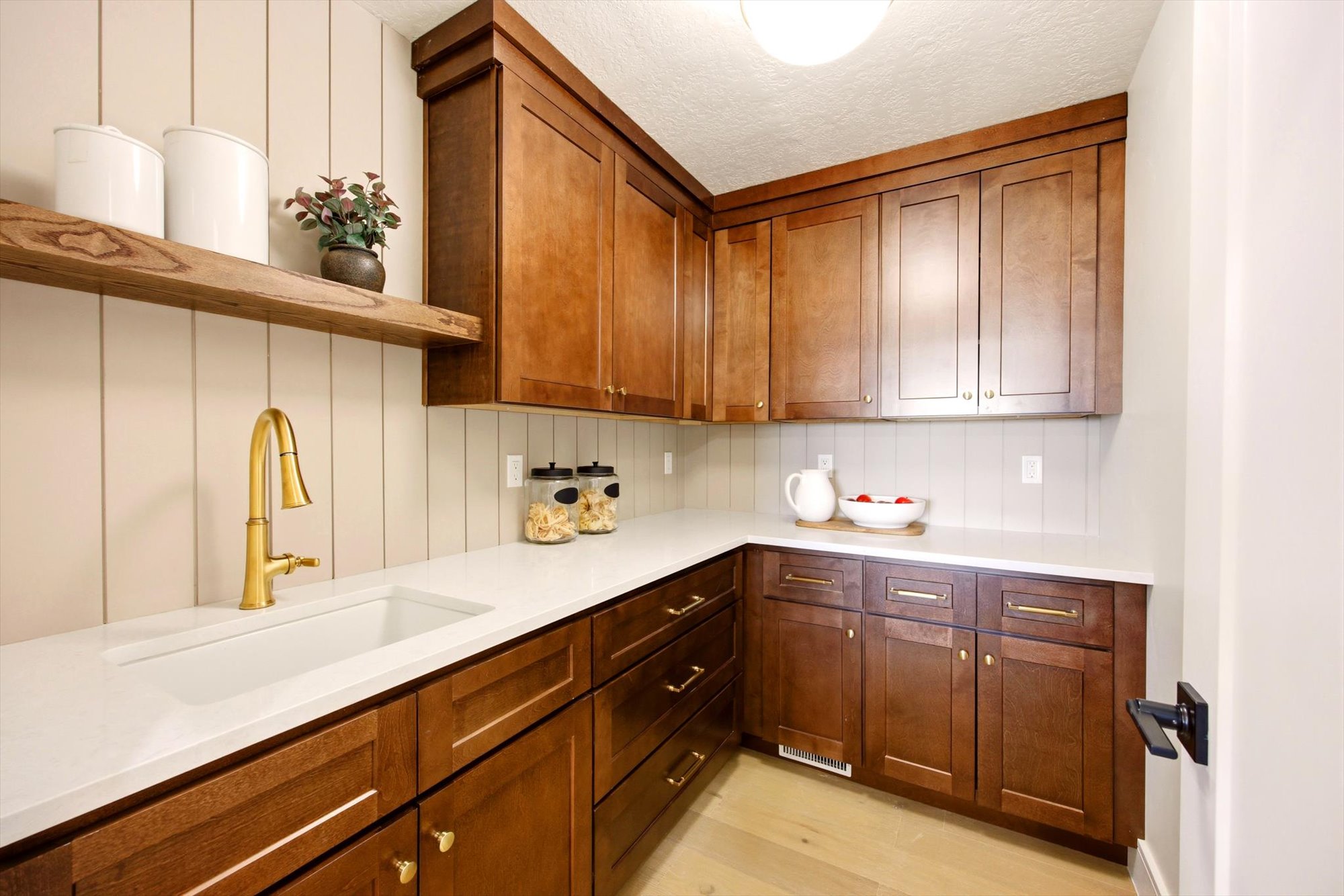 Kitchenette featuring extensive wood cabinetry, white countertops, a large undermount sink with a brass-finish faucet, and a light wood-finish floor