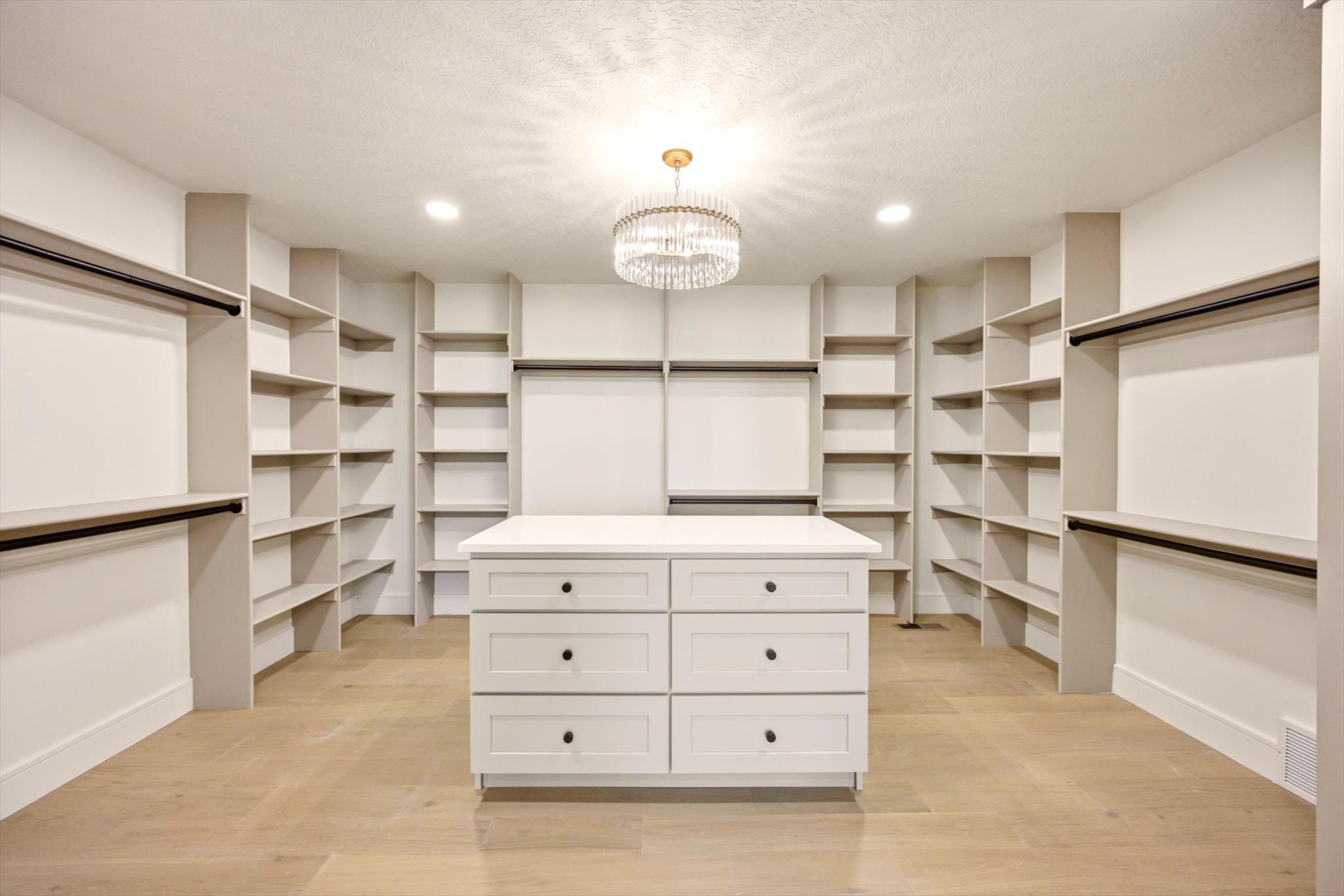 Spacious custom closet featuring extensive built-in shelving, multiple hanging rods, and a central island with six drawers