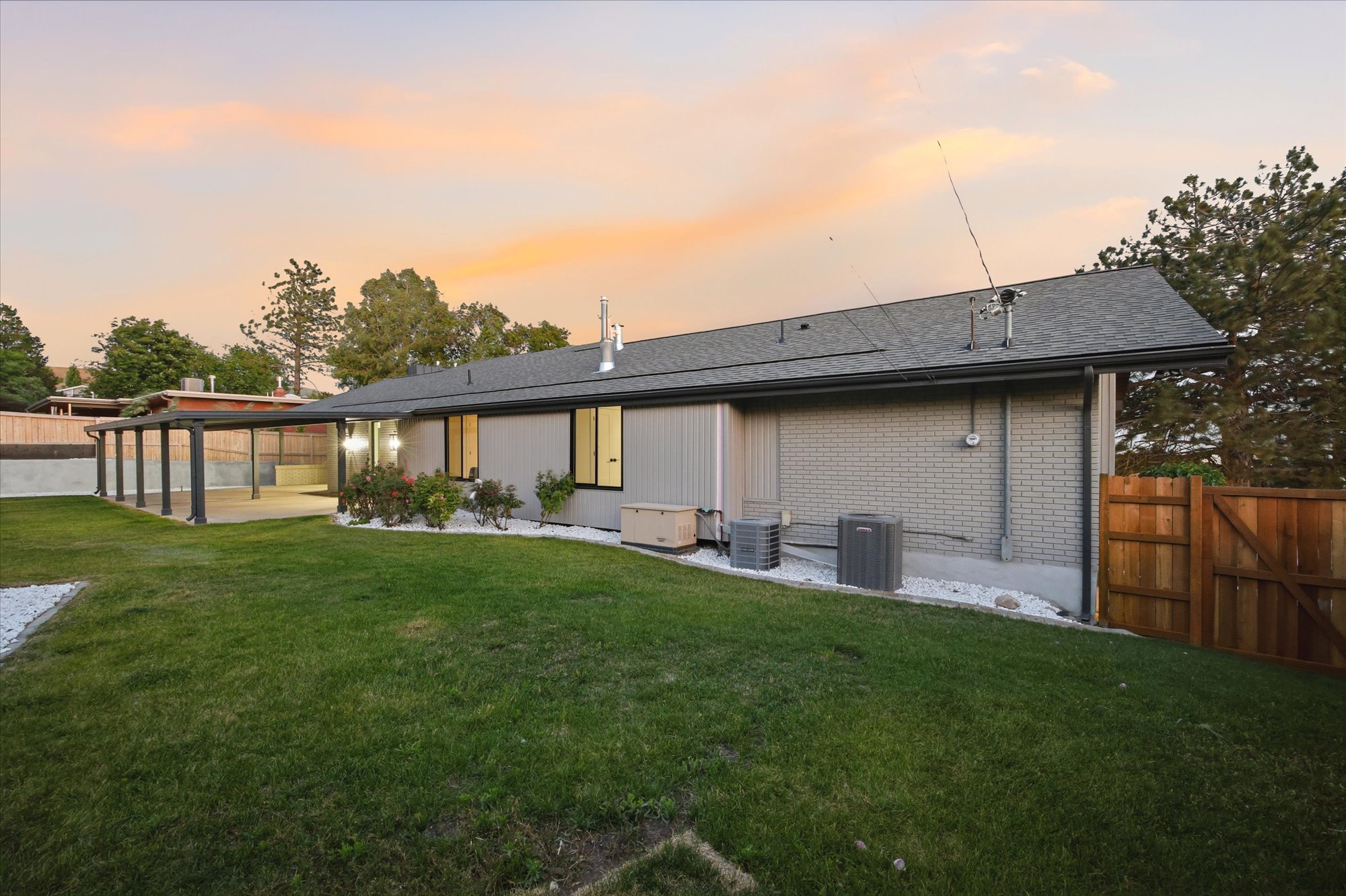 Expansive backyard featuring a manicured lawn, a covered patio structure, and mature landscaping