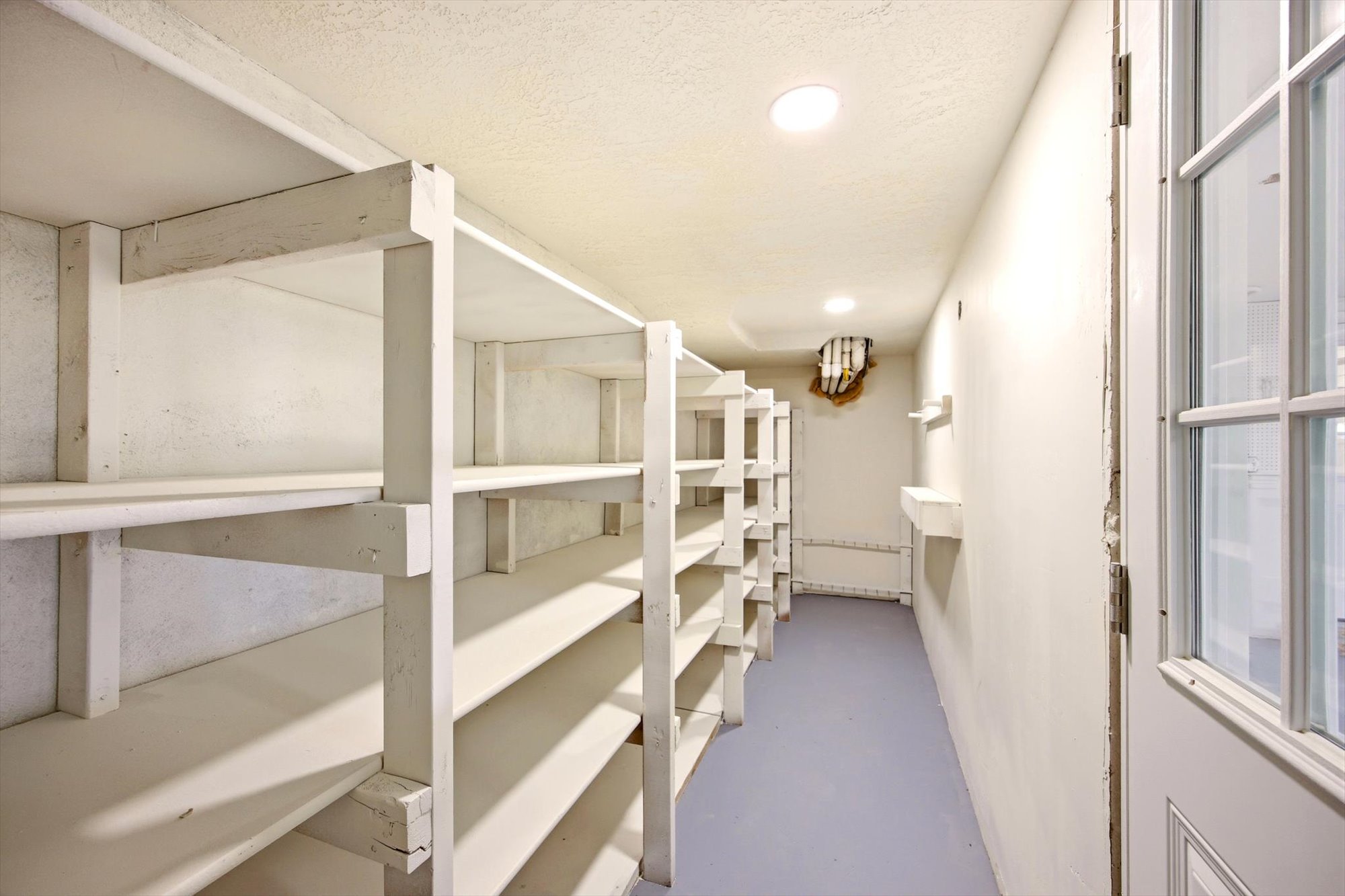 Dedicated storage room featuring extensive built-in shelving, recessed ceiling lighting, and a white paneled door with window panes