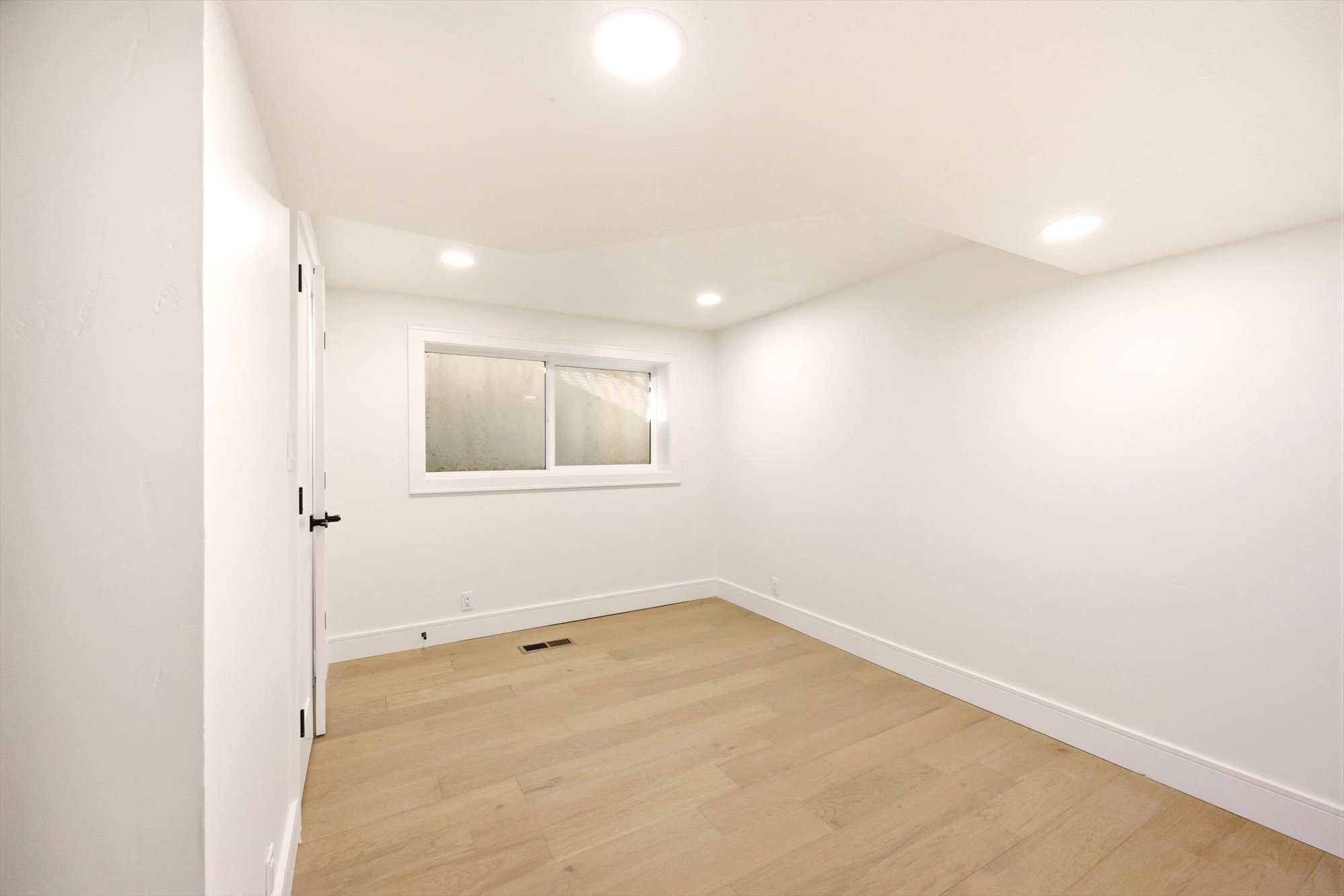 Bright interior space featuring light wood-finish flooring, recessed lighting, and a white framed window