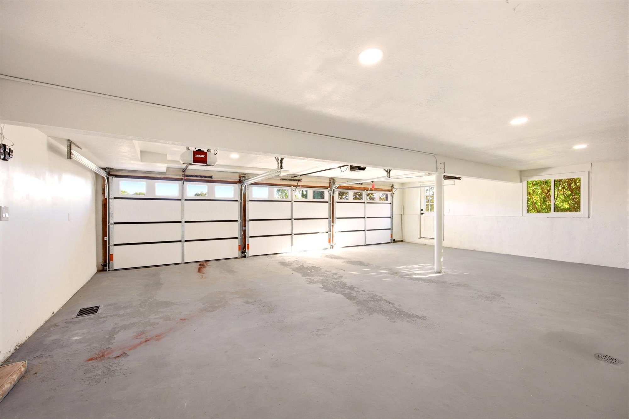 Spacious garage featuring a light gray concrete floor and three overhead garage doors with frosted window panels