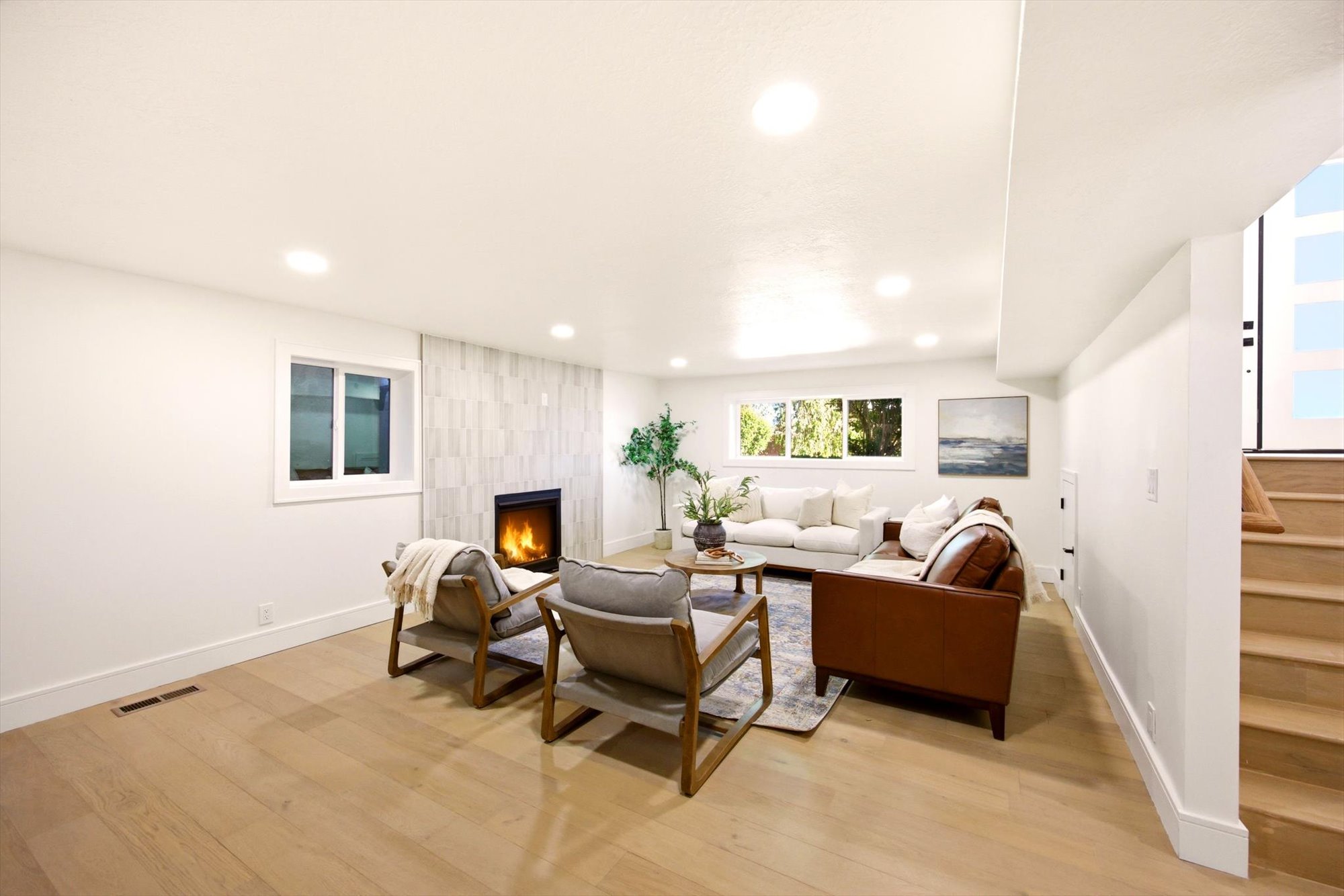 Spacious living area featuring light wood-finish flooring, recessed lighting, and a modern fireplace with a tiled surround