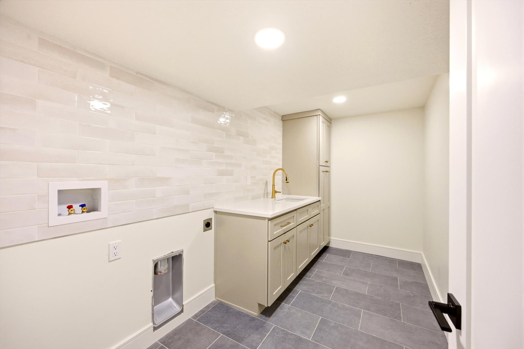 Dedicated utility space featuring a built-in sink with brass hardware, extensive cabinetry for storage, and durable floor tile