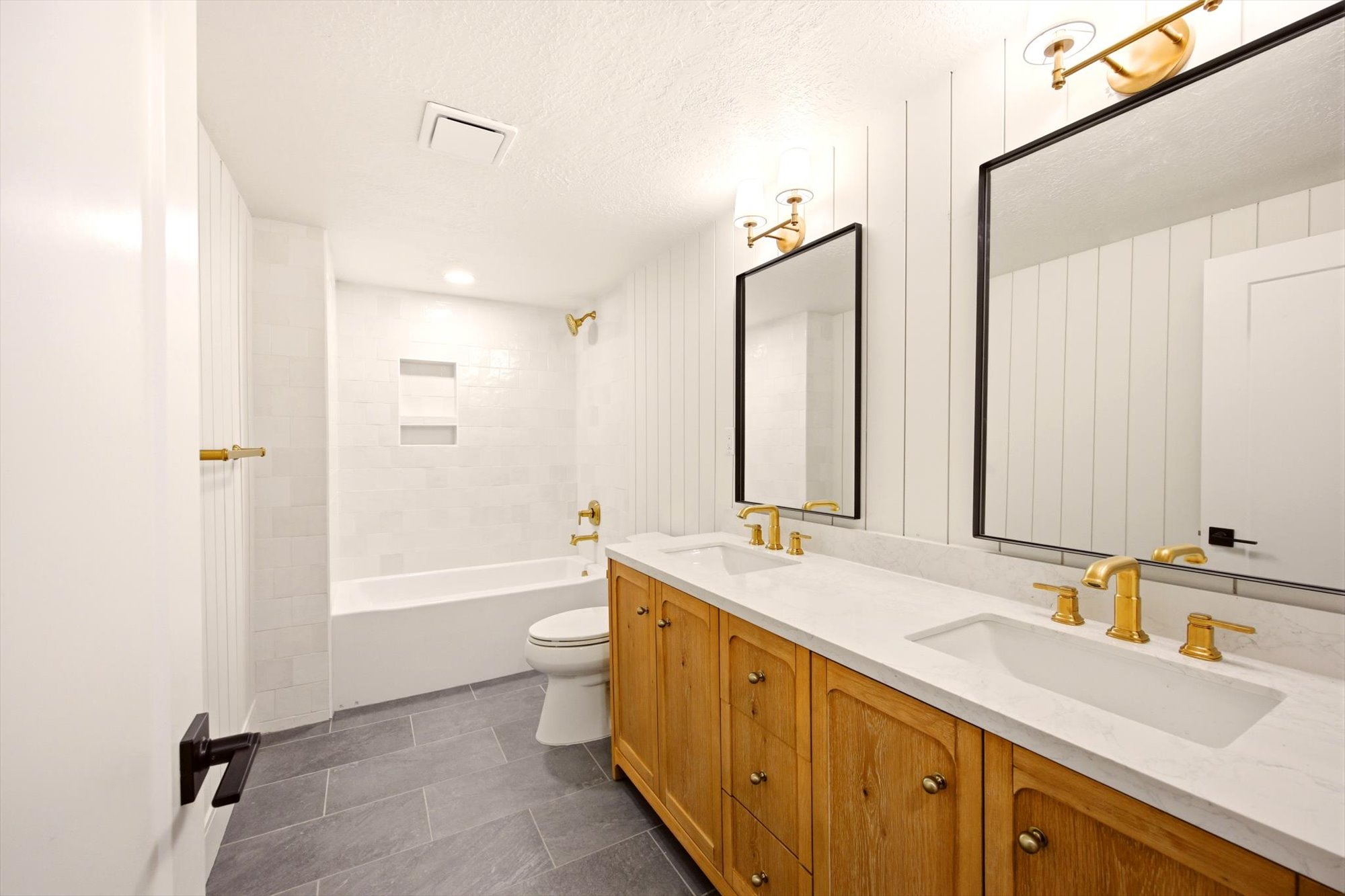 Dual vanity with wood-finish cabinetry, white countertops, and gold-finish fixtures