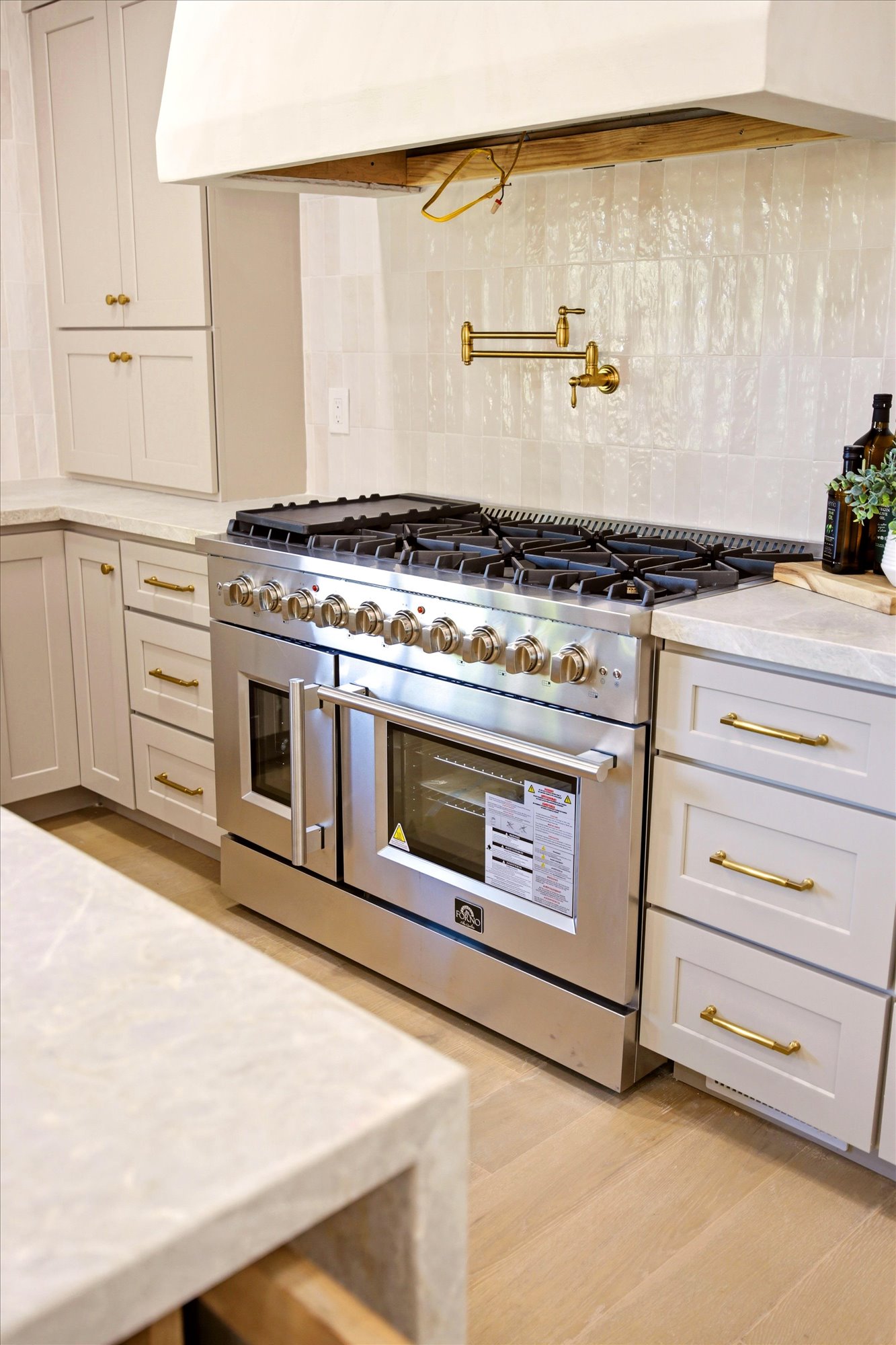 Stainless steel range with a built-in griddle, complemented by a white tile backsplash and a brass pot filler