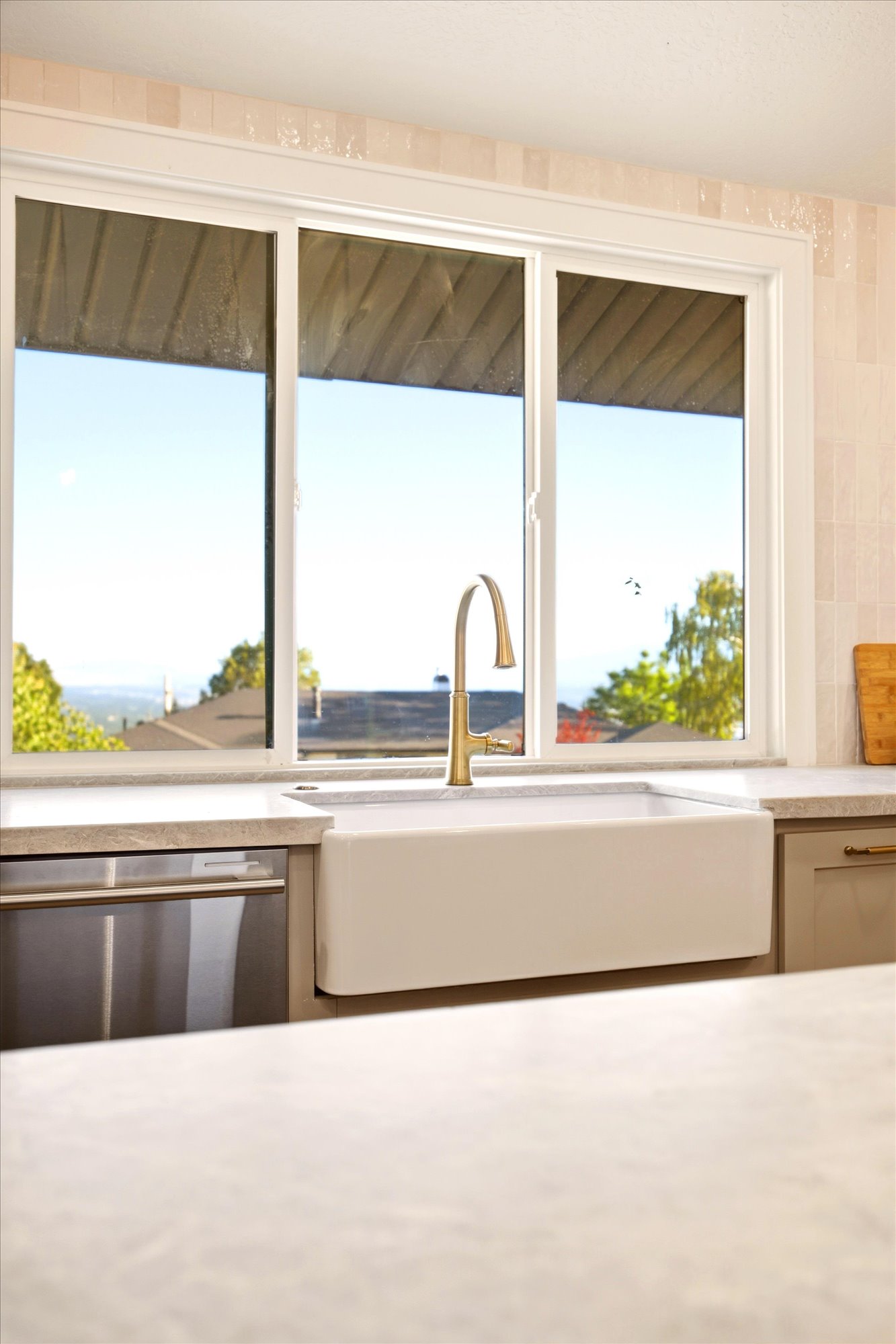 Kitchen sink with a gold-finish faucet, a built-in dishwasher, and a large window