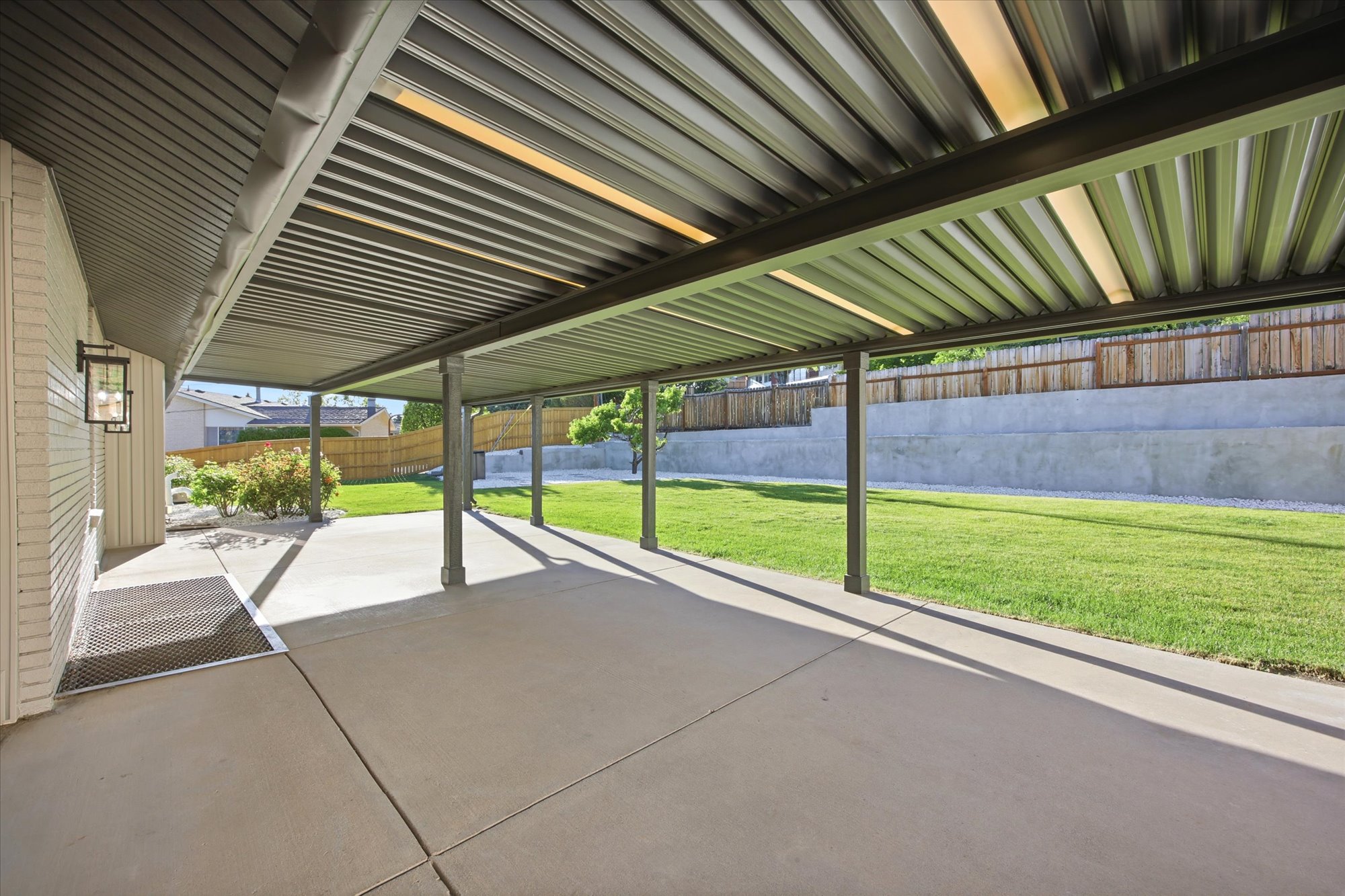 Expansive covered patio featuring a corrugated metal roof with integrated lighting, concrete flooring, and multiple support columns