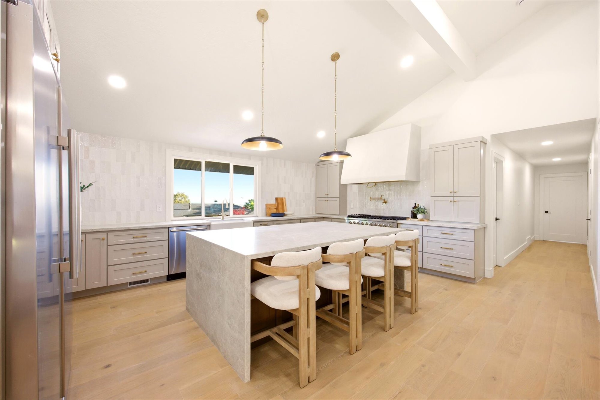 Spacious kitchen featuring a large waterfall island, stainless steel appliances, light wood-finish flooring, vaulted ceilings, and recessed lighting