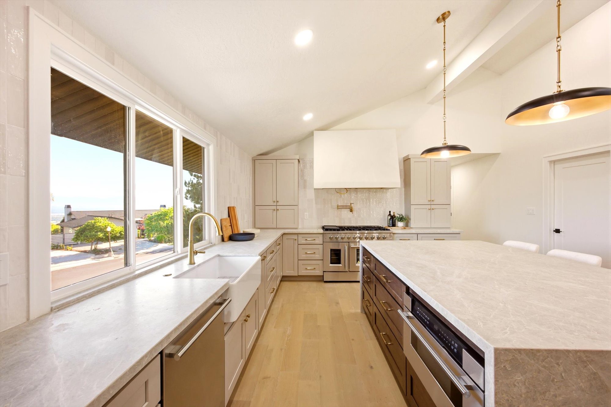 Modern kitchen featuring a large center island with integrated microwave, light wood-finish flooring, vaulted ceiling, and ample natural light from oversized windows