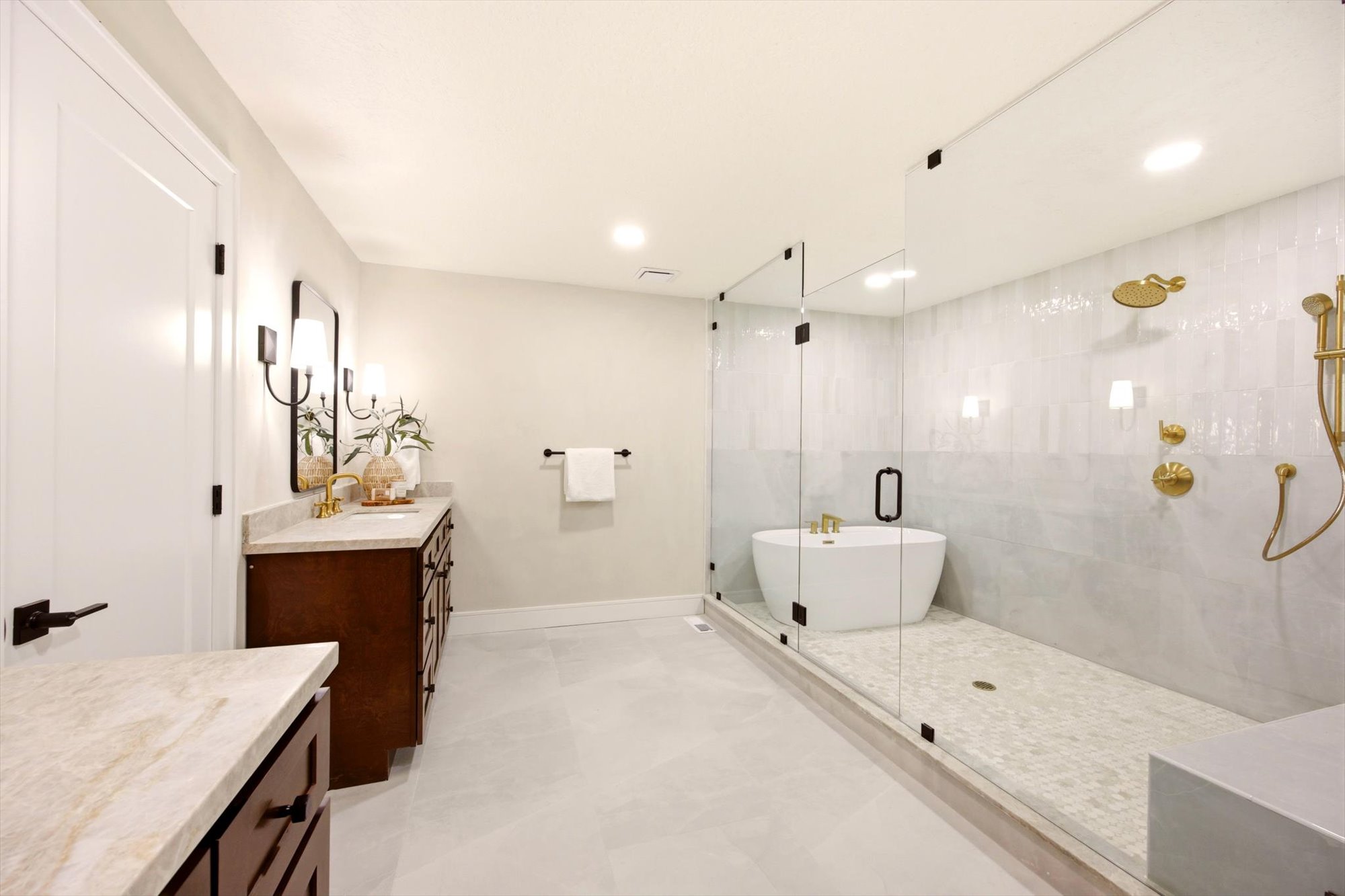 Spacious bathroom featuring a frameless glass walk-in shower with a freestanding soaking tub, dual vanity with stone countertops, and gold-finish plumbing fixtures