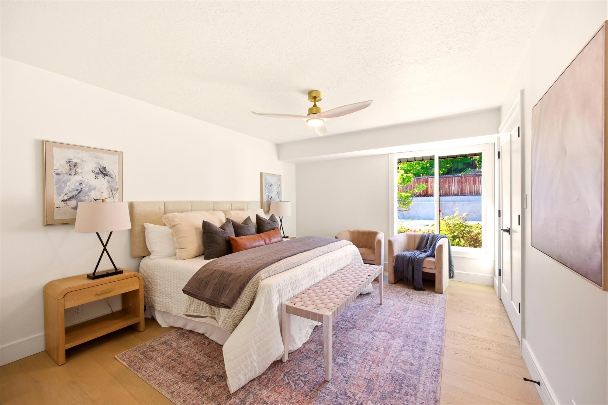 Bedroom featuring light-tone wood-finish flooring, a contemporary ceiling fan with integrated lighting, a large window, white trim, and a white interior door with dark hardware