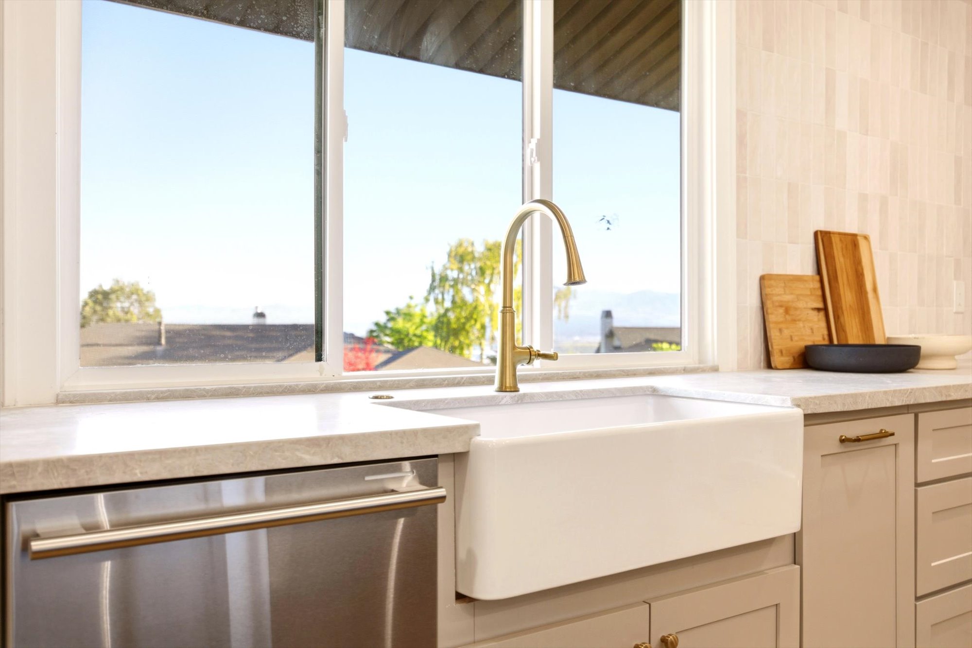 Kitchen featuring a white farmhouse sink with a gold-tone gooseneck faucet, light-toned countertops, and a full-size stainless steel dishwasher