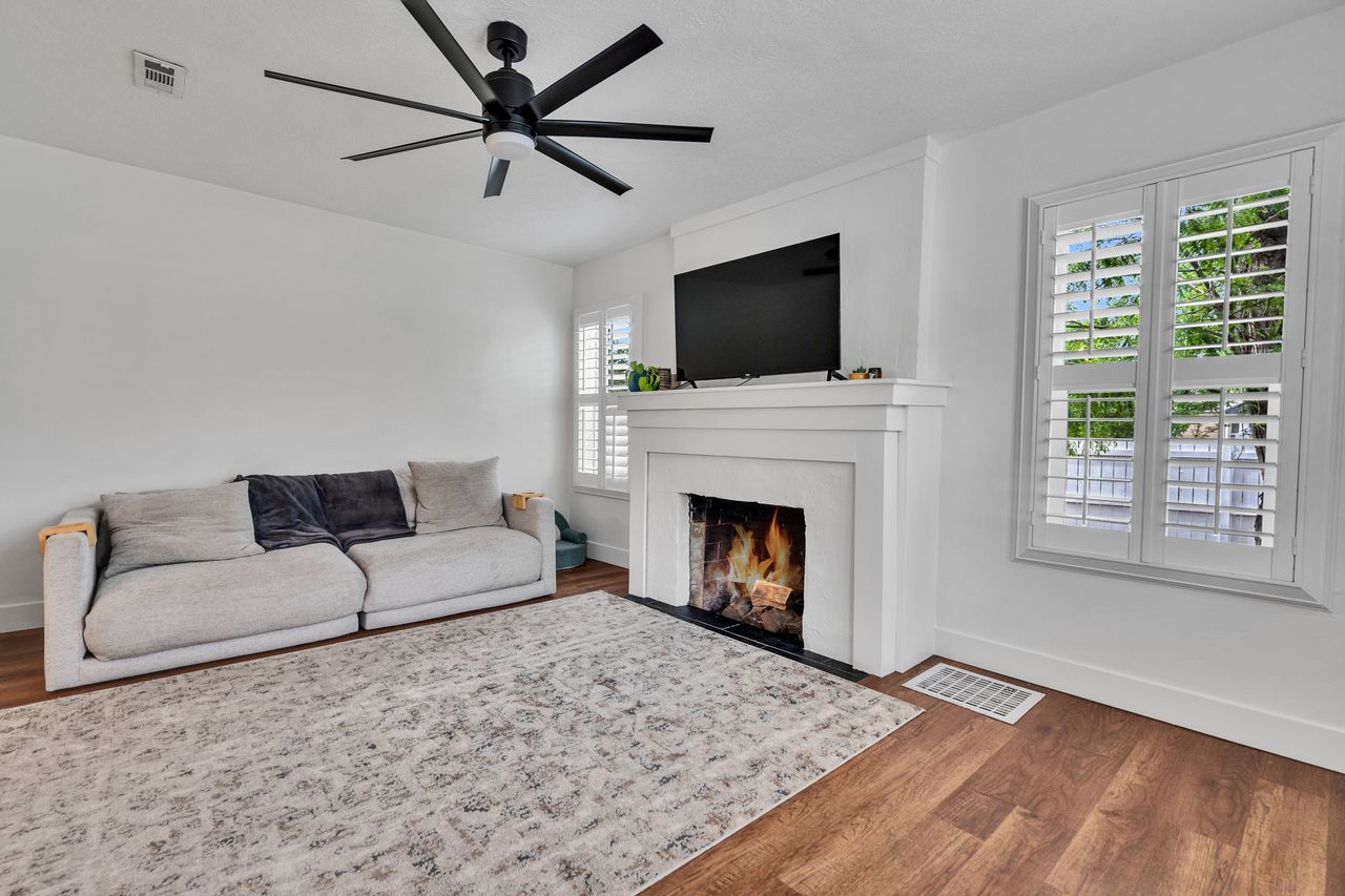 Living area featuring wood-finish flooring, a white fireplace with a black hearth, and plantation shutters